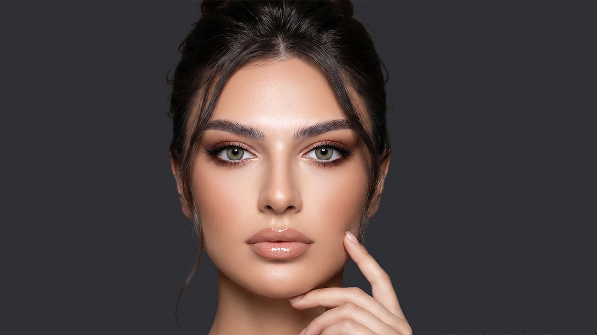 Close-up of a model wearing gray-green colored contact lenses against a dark gray background.